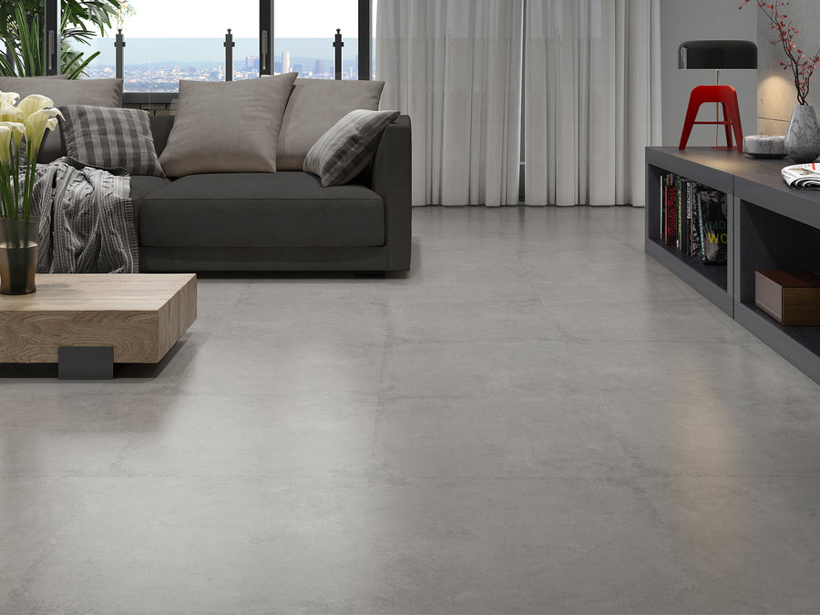 Keramische betonlook tegel in formaat 60x60 cm geplaatst in een living met zetel en grote ramen.