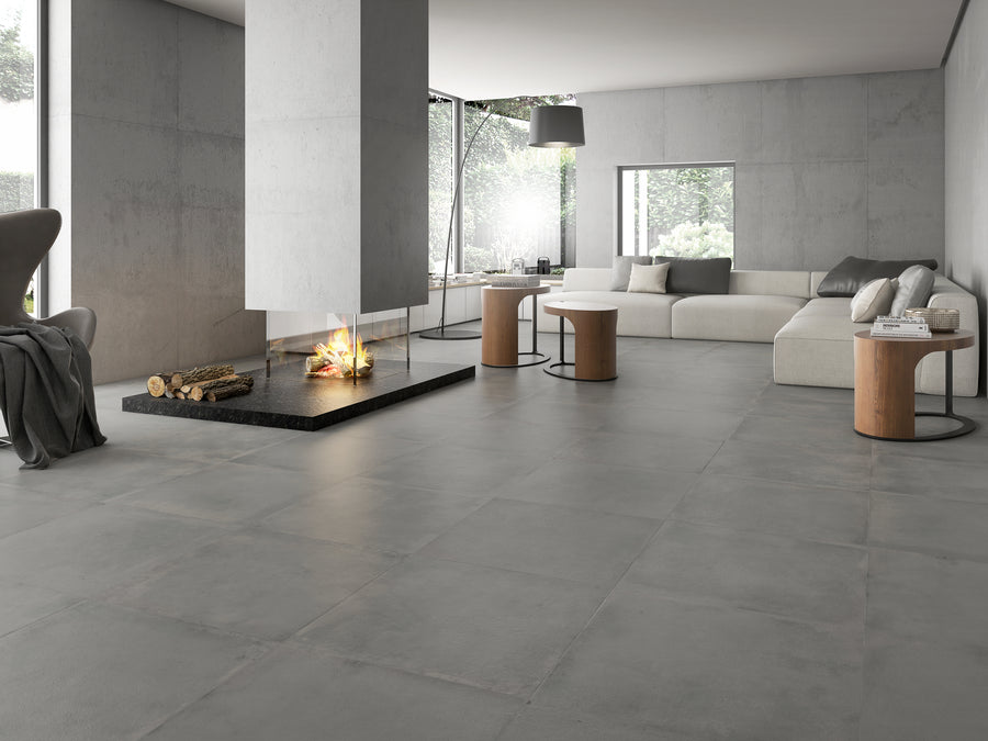 Keramische Grigio tegels met betonlook in formaat 75x75 cm weergegeven in een living met zetel en sfeerhaard. 